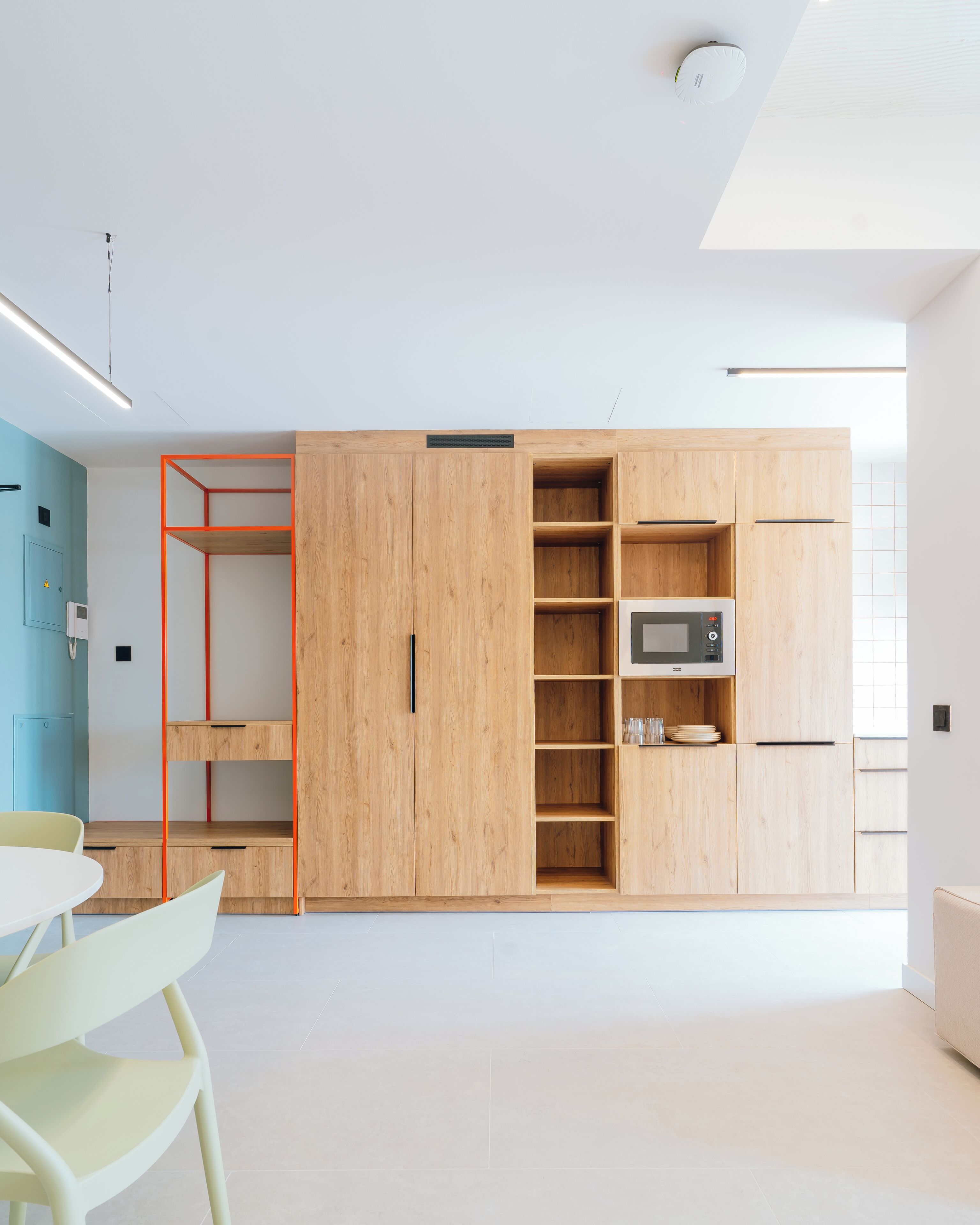 Een moderne keuken met houten kastjes, een magnetron en een klein eethoekje met een tafel en stoelen.