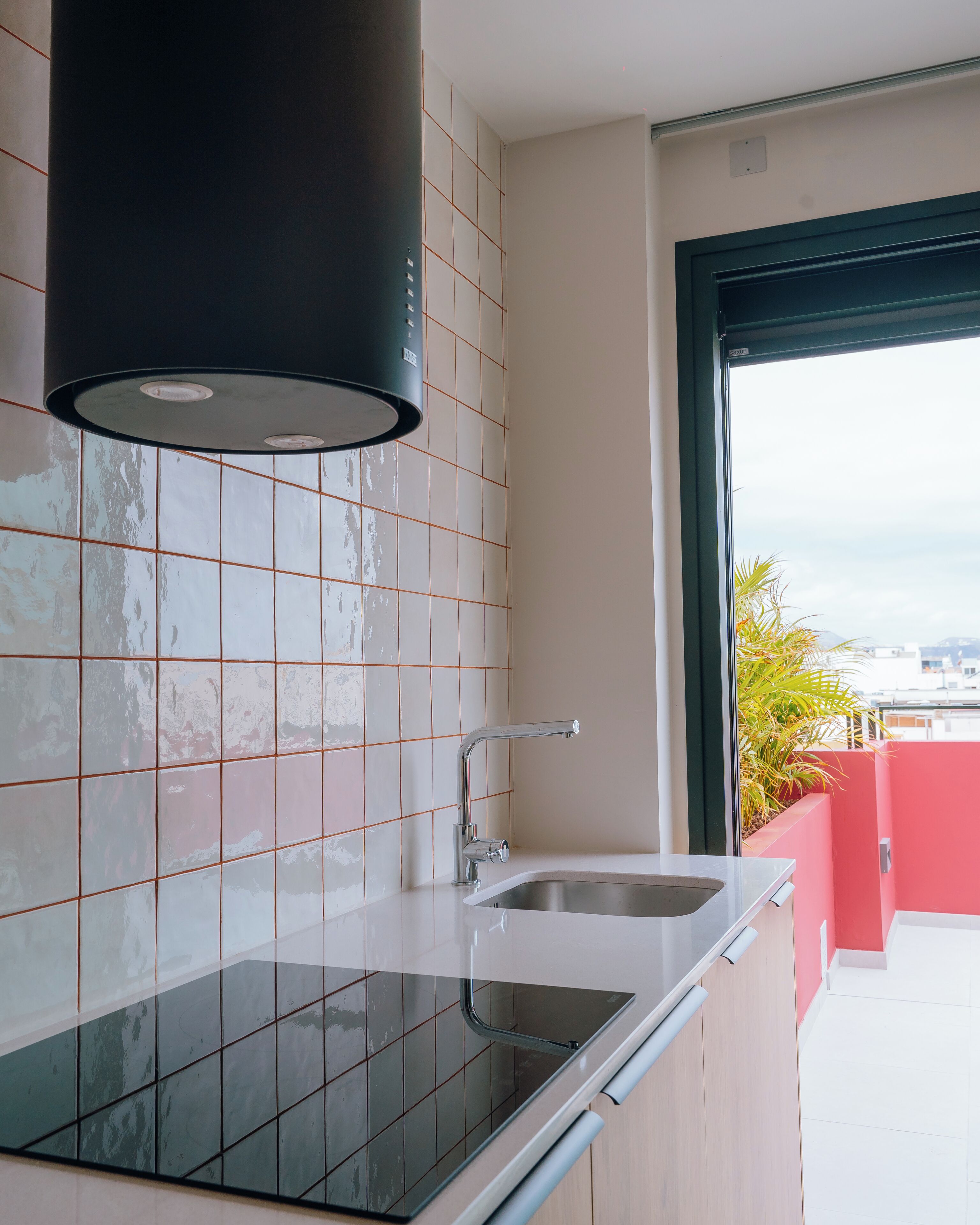 A modern kitchen with a black stove, white tiles, and a window with a view.