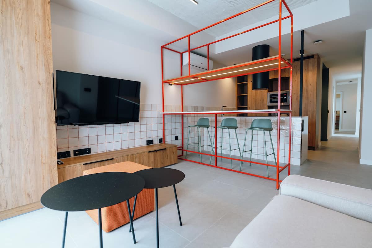 Een moderne keuken met een televisie, een eethoek met krukken, en een rode metalen constructie.