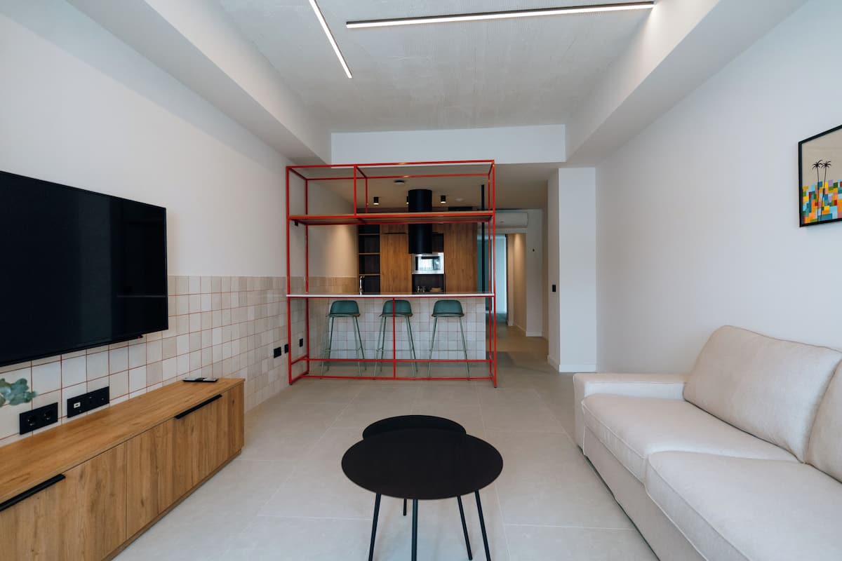 Een moderne woonkamer met een flatscreen-televisie, een bank en een eethoek met stoelen en een rode metalen constructie.