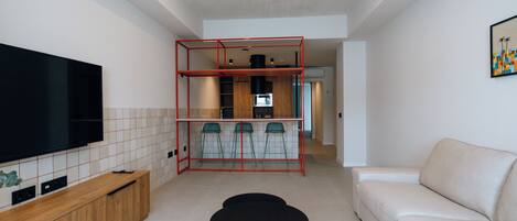 En moderne stue med et fladskærms-tv, en sofa og et spiseområde med stole og en rød metalstruktur.