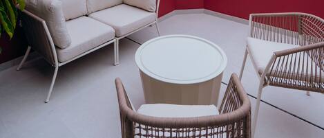 Una terraza en la azotea con un muro rojo, un sofá blanco, sillas de mimbre y una mesa redonda.
