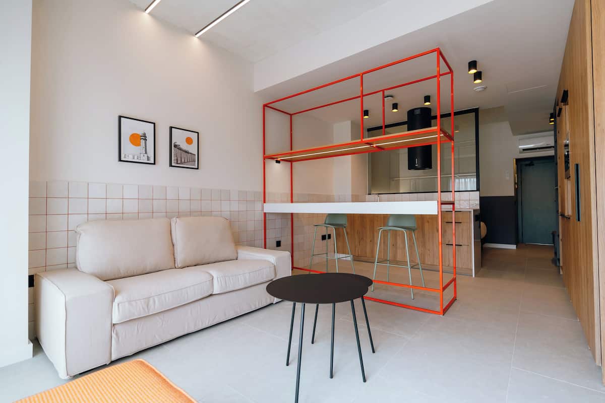 Een moderne woonkamer met een bank, een eethoek met een rode metalen constructie, en een keuken op de achtergrond.