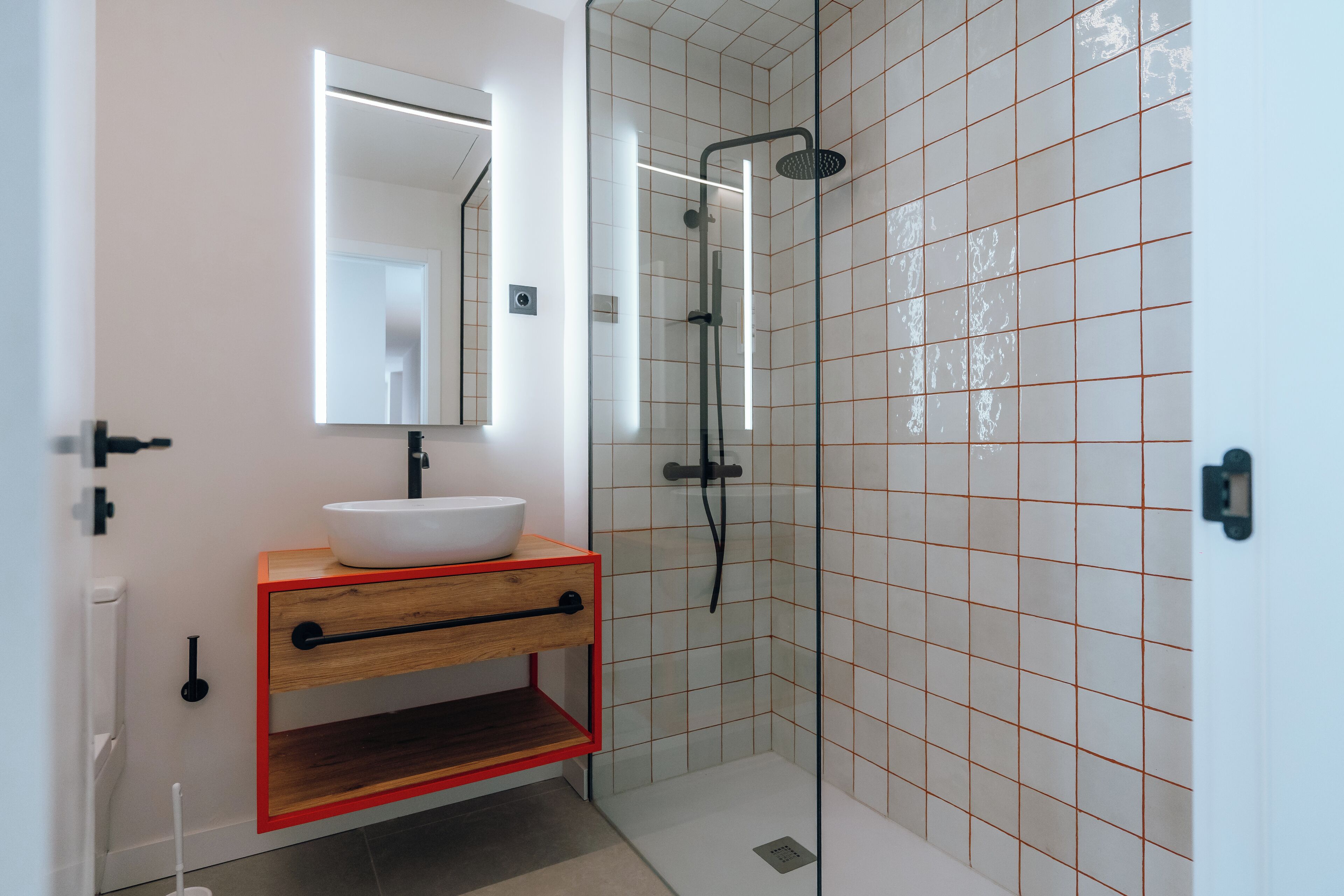 Une salle de bain moderne avec une douche à parois de verre, un lavabo blanc et un meuble-lavabo en bois.