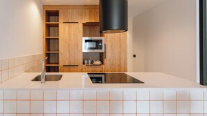 Une cuisine moderne avec des plans de travail blancs, un évier en acier inoxydable, des armoires en bois, un four à micro-ondes encastré et un luminaire suspendu noir.
