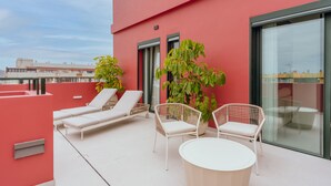 Une terrasse sur le toit avec des chaises longues blanches, un fauteuil en osier et une table ronde.