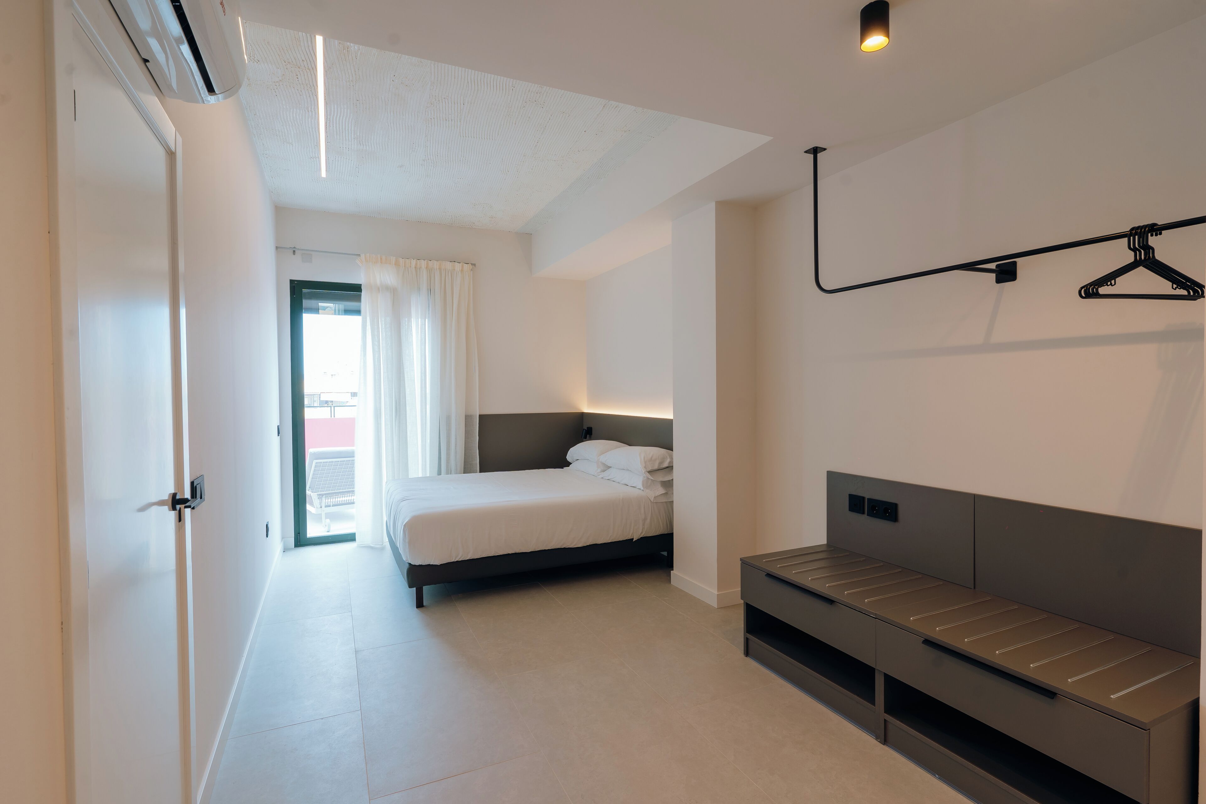 A modern bedroom with a bed, bedside table, and a hanging clothes rack.