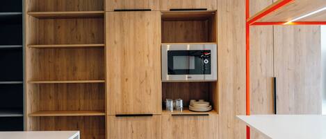 Una cocina moderna con armarios de madera, microondas integrado y encimera blanca.