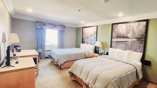 Habitación de hotel con dos camas, un escritorio con computadora y una ventana con cortinas.