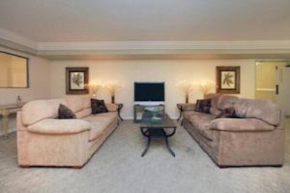 A living room with two beige sofas, a glass coffee table, and framed artwork on the walls. - Super 8 by Wyndham Temple I-35 (Temple)