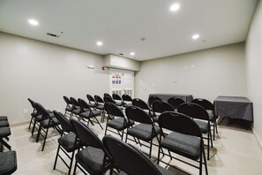 A conference room with rows of chairs, a table, and a door with a poster. - Surestay Studio by Best Western Conroe Downtown (Conroe)