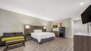 Habitació d'hotel amb llit, escriptori, sofà, cuineta i televisió plana.