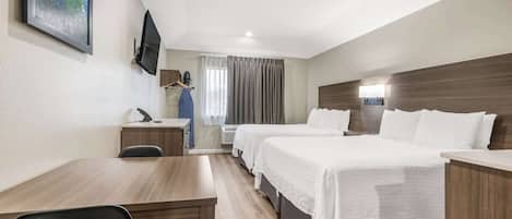 A hotel room with two beds, a desk, a chair, a TV, and a window with curtains.