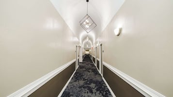 A hotel hallway with a patterned carpet, white walls, and a geometric light fixture.