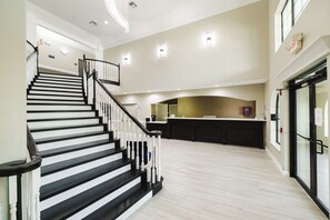 A spacious interior with a staircase leading to a second floor, a kitchen area with a counter, and a glass door entrance. - Surestay Studio by Best Western Conroe Downtown (Conroe)