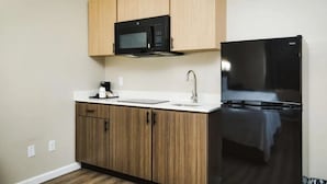Une cuisine de taille réduite avec des meubles en bois, un micro-ondes noir, un réfrigérateur noir et un plan de travail blanc.