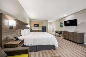 Une chambre d’hôtel comprenant un lit, une table de chevet, une lampe, une télévision, une kitchenette et une petite table avec des chaises.