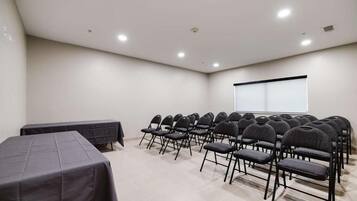 A conference room with rows of chairs and tables, a projector screen, and a whiteboard.