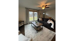 Ein Wohnzimmer mit einem dunkelgrauen Sofa, einem Holztisch und einem Deckenventilator.