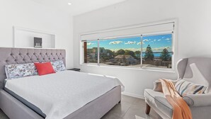 A bedroom with a large bed, a window with a city view, and a chair with a blanket.