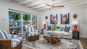 Sala de estar com sofá, poltronas, mesa de centro e vista para o oceano através de grandes janelas.