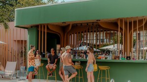 Een bar bij het zwembad met een groene wand, houten latten en diverse flessen en glazen.