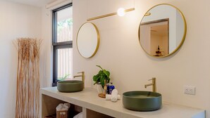 Een moderne badkamer met twee ronde wasbakken, een grote spiegel en een raam.