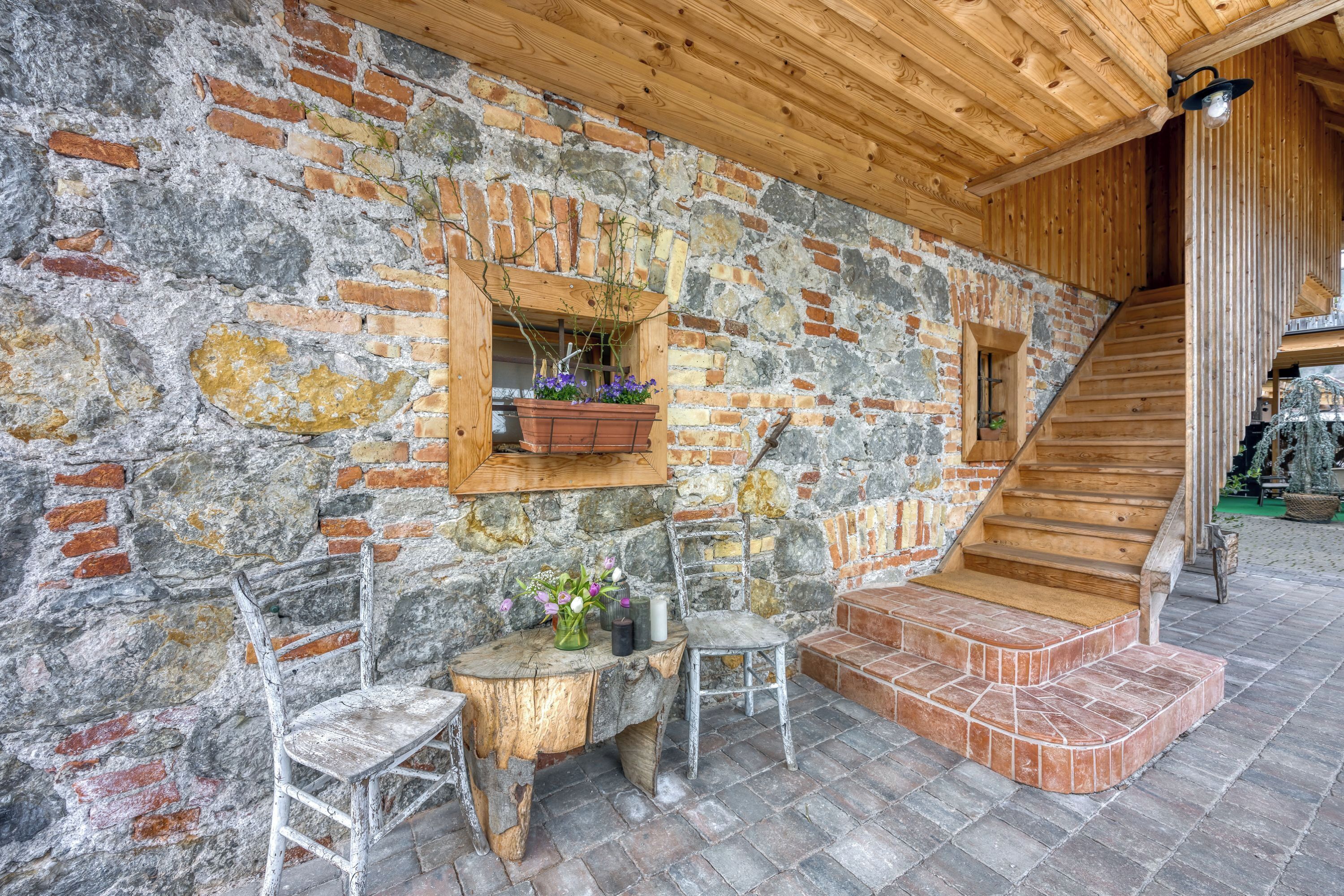 Una pared de piedra rústica con una escalera de madera, una mesa de madera con una silla y una maceta colgante.