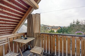 A wooden balcony with a table and chair, overlooking a residential area.