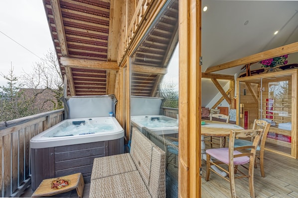 A wooden deck with hot tubs, wicker furniture, and a glass-enclosed dining area.