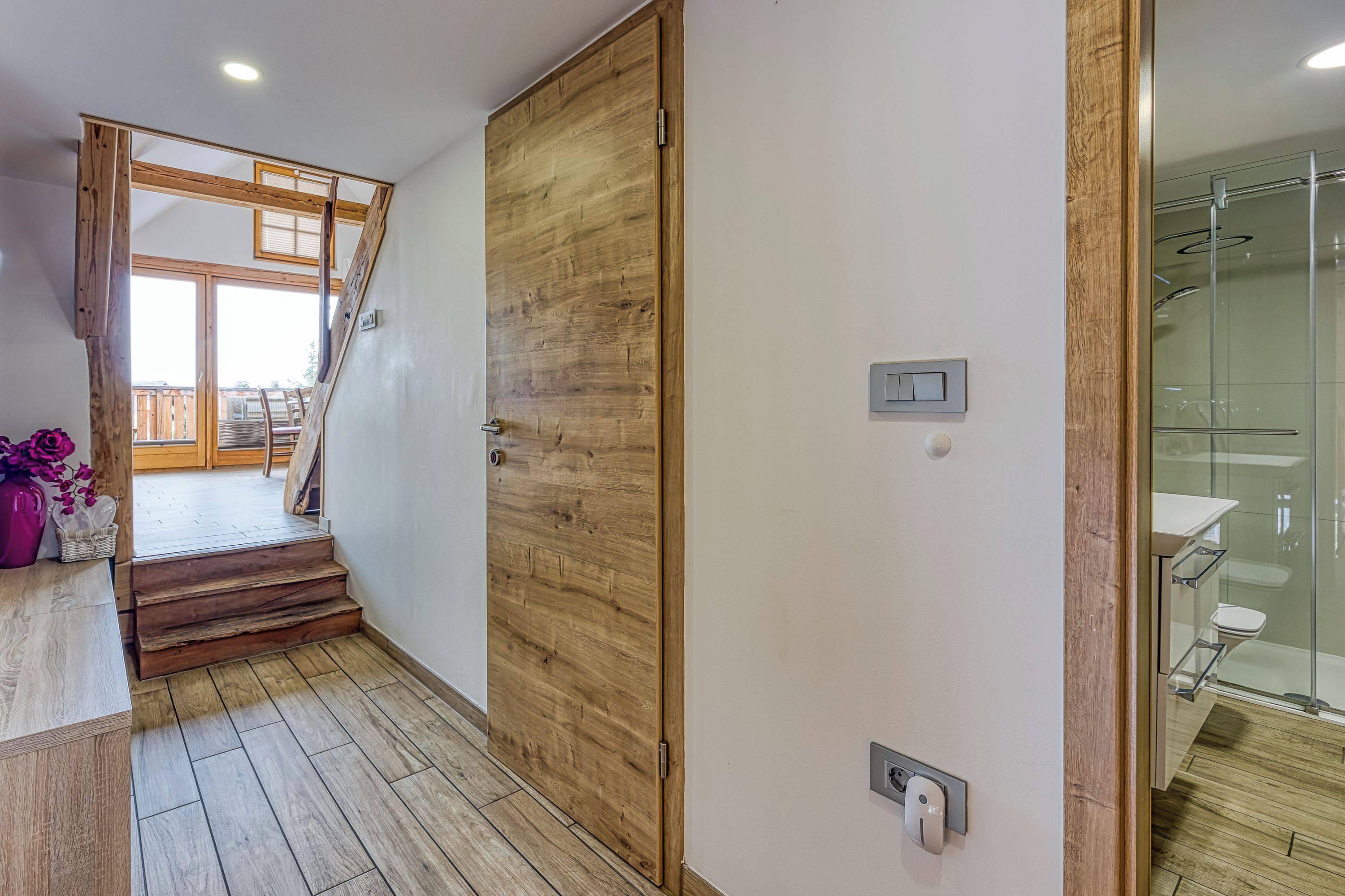 Une porte en bois donne accès à une salle de bain dotée d’une cabine de douche en verre.