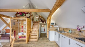Et moderne loftværelse med trappe i træ, et lille tekøkken og et badeværelse med bruser og toilet.