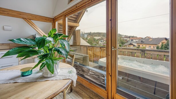 En balkon med et spabad, et træbord med en plante og udsigt til huse i baggrunden.