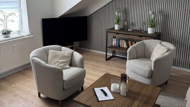 Una sala de estar moderna con dos sillones, una mesa de centro, una estantería y un televisor.