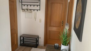 Un pasillo con puerta de madera, un perchero, un banco, una alfombra blanca y una planta en maceta.