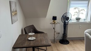 Un dormitorio estilo loft acogedor con techo inclinado, una mesa de comedor con sillas, un ventilador de pie y una ventana con vistas a zonas verdes.