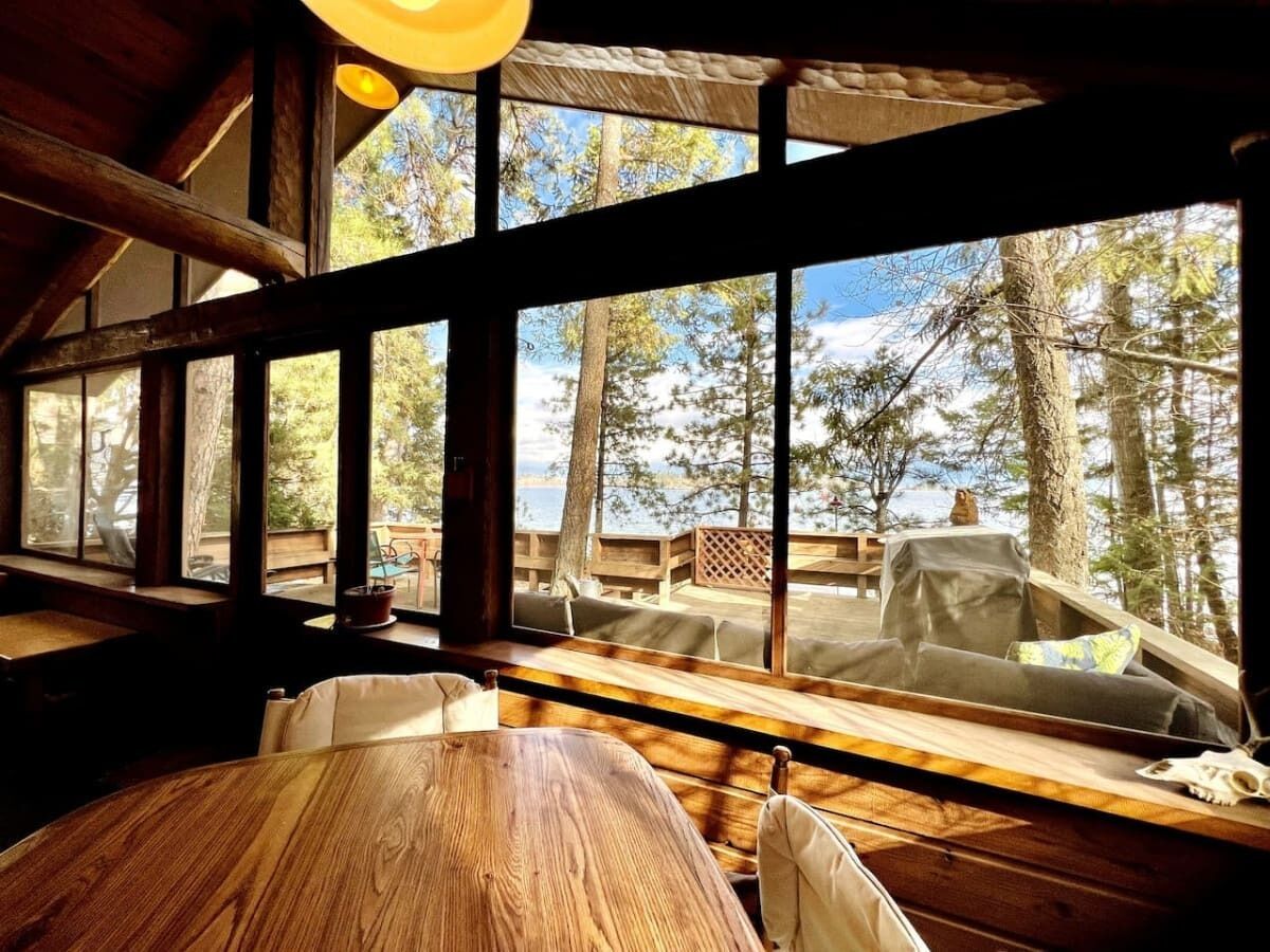 A rustic cabin interior with large windows overlooking a deck and forest.