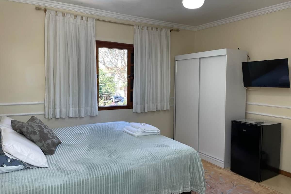 Quarto com cama, cortinas, uma TV e um pequeno eletrodoméstico preto.