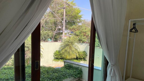 Quarto com porta de correr de vidro que dá para uma varanda com chão em mosaico e um pequeno jardim.