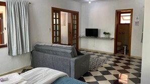 Quarto com uma cama, um sofá cinza, uma televisão e piso xadrez.