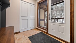 A hallway with a wooden floor, a black doormat, and a white door with a glass panel. - Algonquin by RVMT (Mont-Tremblant)