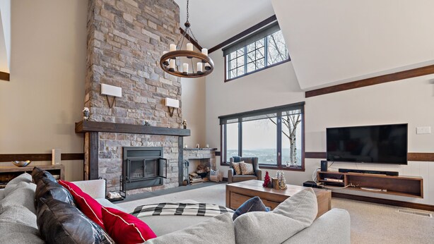 A spacious living room with a stone fireplace, a large window, and a flat-screen TV. - Algonquin by RVMT (Mont-Tremblant)