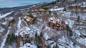 A snow-covered resort with multiple buildings, including a large lodge with balconies and a smaller cabin-style structure. - Algonquin by RVMT (Mont-Tremblant)