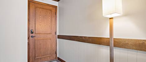 Un couloir avec une porte en bois, un luminaire et un mur blanc orné d’une moulure en bois.
