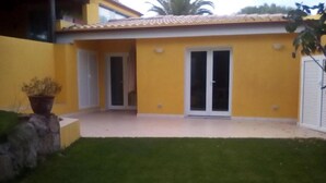 A yellow building with a tiled roof, a glass door, and a small garden area with a stone wall and a potted plant. - Apartment in Sardinia near Surf Paradise (Porto Pollo)