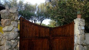 A rustic wooden gate with a stone wall on either side, leading to a property with a yellow building in the background. - Apartment in Sardinia near Surf Paradise (Porto Pollo)