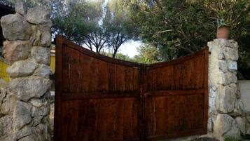 A rustic wooden gate with a stone wall on either side, leading to a property with a yellow building in the background.