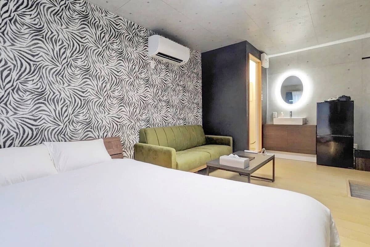 Ein Hotelzimmer mit einem großen Bett, einem grünen Sessel, einem kleinen Tisch, einem Spiegel und einem schwarzen Kühlschrank.