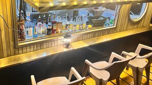 A bar area with a glass display case containing various bottles, a small table with a lantern, and plastic chairs. - Yonaguni-mumbu Airport Hotel (Yonaguni)