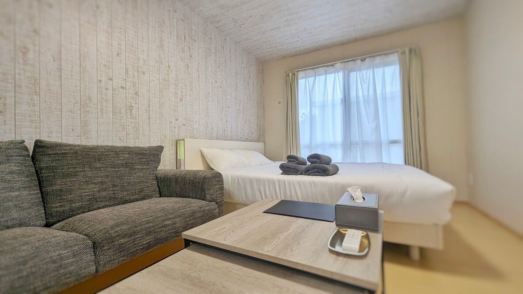 A hotel room with a sofa, a bed, a bedside table, and a window with curtains.